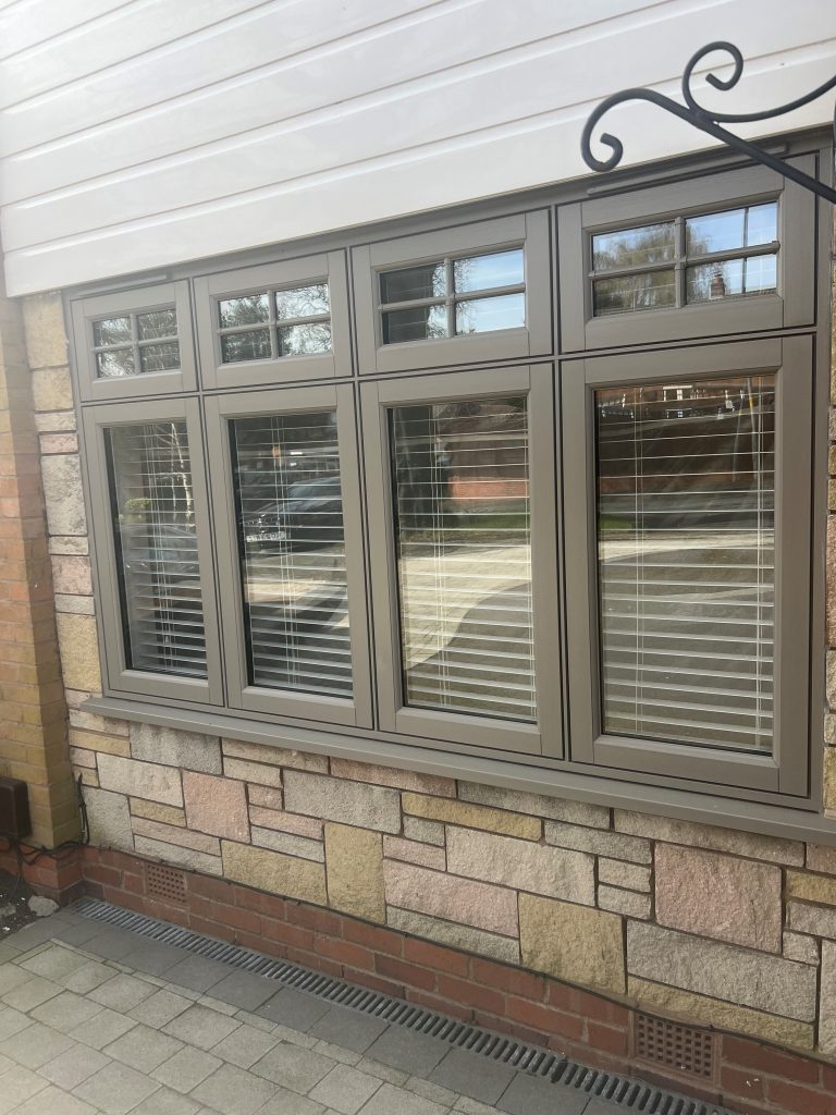 Modern Agate Grey UPVC casement windows with Georgian bar top lights and integrated white Venetian blinds, installed in a home with natural stone cladding and white weatherboard siding.